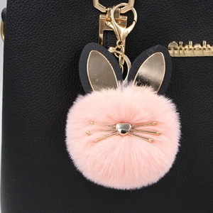 Pink plush rabbit fur ball keychain with gold ears hanging on a black leather handbag