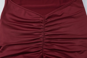 Dettaglio dell'abito aderente rosso vino con eleganti arricciature e tessuto lucido