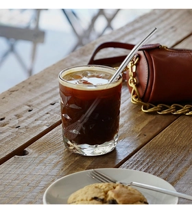Detail of stainless steel 2-in-1 straw spoon stirring an iced coffee in a textured glass