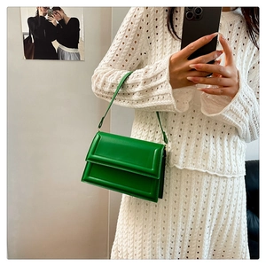 Green leather small square bag with shoulder strap held by model in white knit outfit