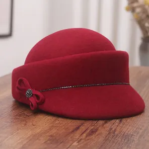 Elegant wine red wool felt equestrian hat with bow and rhinestone detail on wooden desk