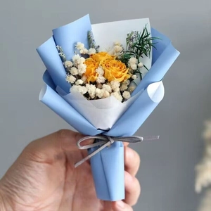 Close-up of mini bouquet with yellow dried roses, gypsophila and light blue paper wrap