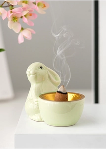 Detail of green ceramic rabbit incense burner with burning cone and rising smoke