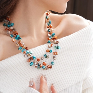 Detail of a layered beaded necklace featuring teal and orange shell fragments on a model