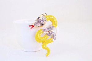 Detail of yellow enamel snake keychain with rhinestones on a white porcelain cup edge