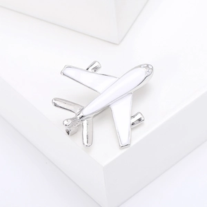 Macro shot of silver airplane brooch with white enamel detail on white geometric stone