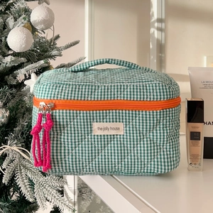 Detail view of a quilted green and white checkered makeup bag with orange zippers
