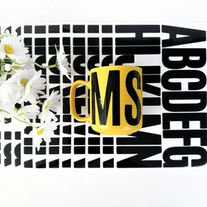 Top view of a bright yellow ceramic mug with bold black MS letters and daisy decor