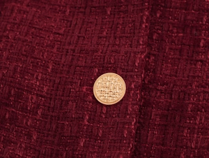 Makroaufnahme eines goldenen Knopfes auf burgunderrotem Tweed-Stoff am V-Ausschnitt Kleid
