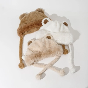 Close-up of thick plush bear ear hats in coffee, white, and beige with soft pompom ties
