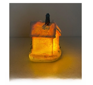 Side view of a glowing Christmas resin house decoration with warm LED lights and faux snow