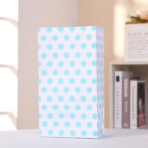 Détail d'un sac cadeau en papier blanc à pois bleu clair dans un décor d'intérieur doux
