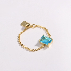 Detail of 18K gold chain ring featuring rectangular blue zircon and heart charm
