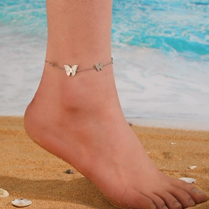 Silver titanium steel butterfly anklet worn on ankle with beach and ocean background