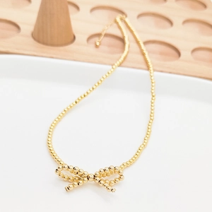 Collana di perline fatta a mano con fiocco in oro 18K presentata su un piatto bianco