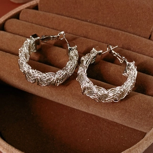 Macro shot of intricate woven silver mesh circular earrings on brown velvet jewelry box