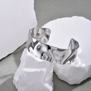 Detailed view of silver stainless steel open bangle with hammered wavy texture on white stones