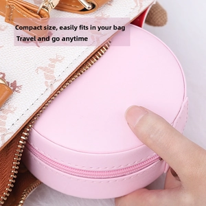Pink round leather travel jewelry case shown fitting easily inside a daily handbag