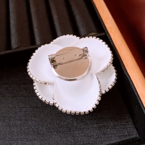 Close-up of white fabric camellia brooch with sparkling rhinestones on black velvet tray