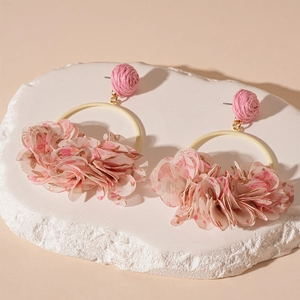 Detail of pink fabric flower earrings with woven spheres on a textured display