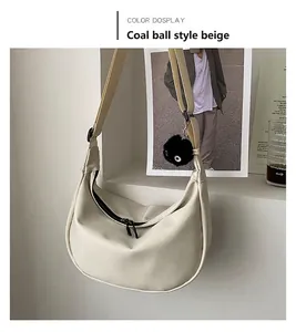 Detail of hobo bag in cream white with a black fluffy pompom charm and zipper closure