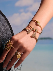 Detail of high-quality zircon gold bangles and rings shown on hand against a sea backdrop