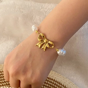 Long tassel pearl necklace with golden bow heart design shown on wrist