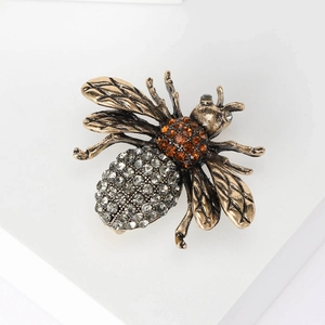 Close-up of a bronze bee brooch with grey and brown rhinestones on a white base