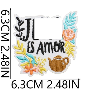 Detail of flower and teapot embroidered patch with ES AMOR text on white background