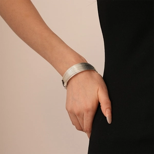 Close-up of a wide silver multi-wire cuff bracelet on a model's wrist with black dress