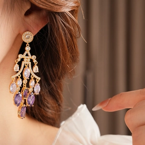 Close-up of model wearing gold tassel earrings with teardrop purple and clear stones