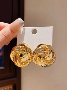 Close-up of golden woven knot stud earrings with a thick metallic twist design
