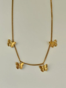 Detail shot of golden butterfly necklace showing four engraved pendants on a delicate chain