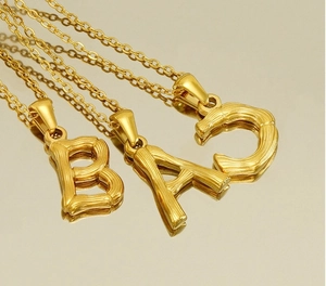 Detailed view of three gold bamboo-style letter pendants A, B, and C on a mirror surface