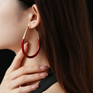 Close-up of model wearing a large gold and burgundy oval enamel stud earring