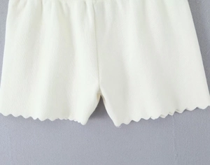 Detail der weißen Rippstrick-Shorts mit dekorativem gewelltem Wellenrand am Saum