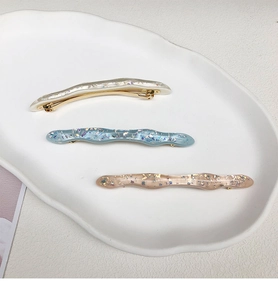 Dettaglio di tre fermagli per capelli a onda in acetato con foglia d'oro