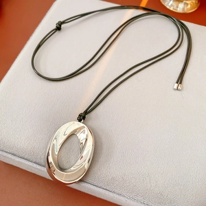 Close-up of polished silver oval pendant on black leather cord over velvet pad