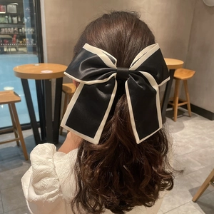 Detail shot of a large black satin bow hair tie with white edges on a low ponytail