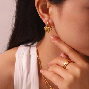 Detail of model wearing 14k gold plated heart earrings and greek key rings set