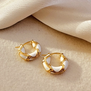 Close-up of 18K gold earrings featuring textured white enamel inlay and woven pattern