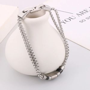 Dettaglio del bracciale a catena in acciaio argentato su un vaso di ceramica bianca