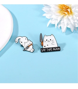 Macro view of white cat enamel pins with knives and Say That Again text slogan