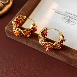 Detail view of gold-plated rose earrings with brown rhinestones on velvet stand