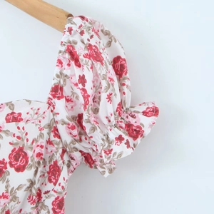 Detailansicht der Puffärmel und rosa Blumenmuster auf weißem Stufenkleid