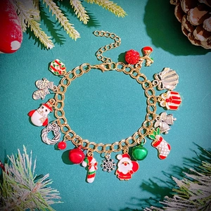 Detail of festive gold bracelet with Santa, snowflake, and bell charms on pine background