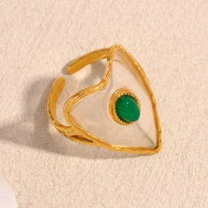 Detail of an 18K gold plated heart ring with a green gemstone on a textured background