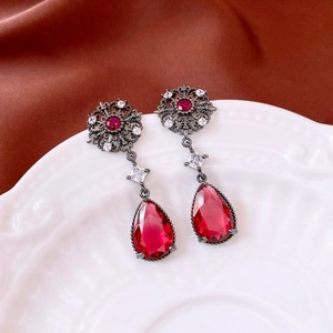 Detail view of vintage-style flower earrings with red stones on an elegant porcelain dish