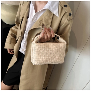Detail of a beige woven mini pillow bag held by a model wearing a stylish trench coat
