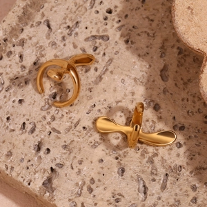 Detailed view of polished 18K gold plated cross ear cuffs on natural stone background